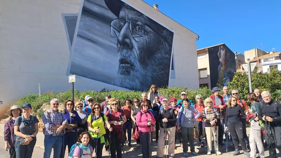 Grupo de personas con ropa deportiva. En el fondo fachada de edificio con la imagen de un señor mayor con gafas