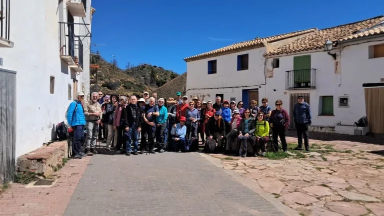 Grupo de personas posando en grupo en la calle de un pueblo con casas blancas de fondo