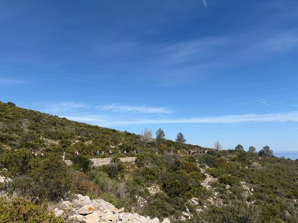 Paisaje de montaña donde se ve a personas andando bajo un cielo azul