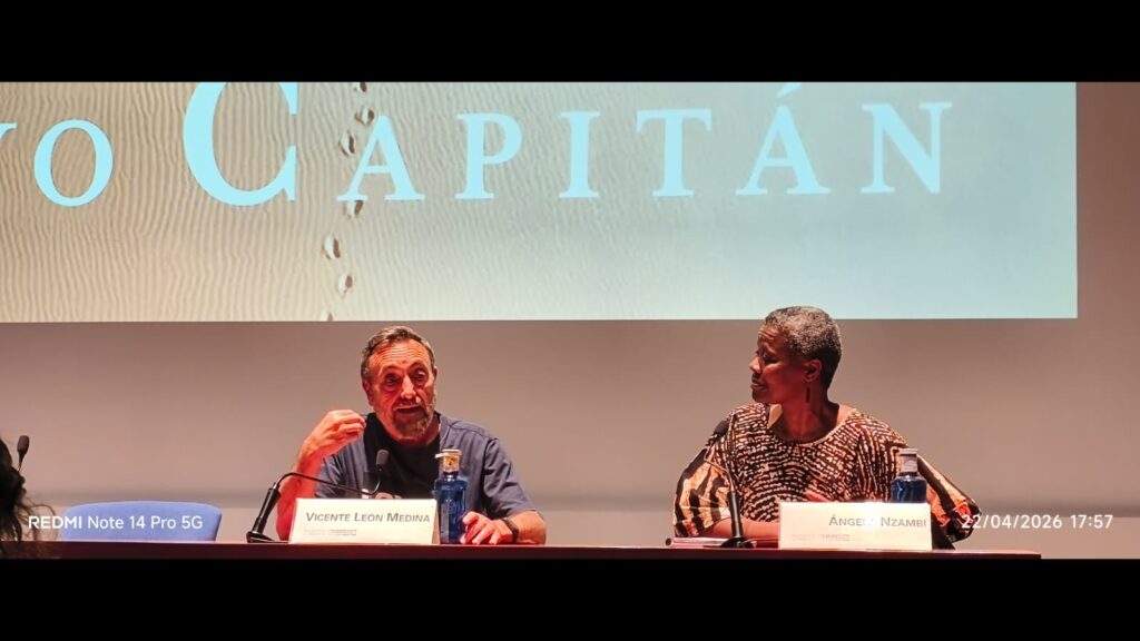 Hombre y mujer ponentes sentados delante de una pantalla con la proyección "Yo capitán"