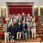 Grupo de personas mayores posando en unas escaleras enmoquetadas sojas