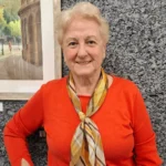 Mujer con suéter naranja y pañuelo al cuello. Fondo negro y gris