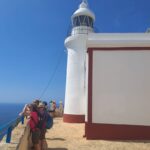 Faro blanco en cielo azul y personas mirando