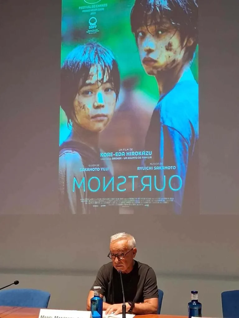 Hombre mayor en sala de ponencias con imagen de película proyectada después
